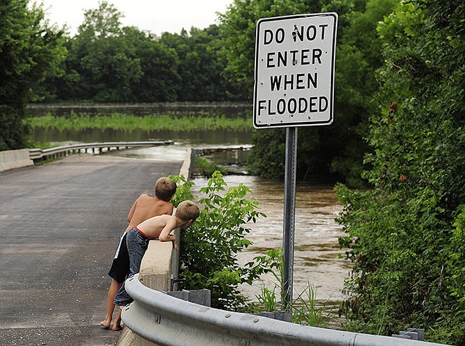 Brothers Kasten and Kelten Baur lean over for a closer look at the swollen Moreau River as it rushes under the Loesch Road bridge on Wednesday afternoon. Just a few feet north of the bridge, the river had already rendered parts of the road impassable and closed to through traffic.