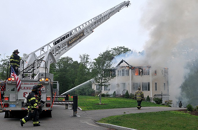 Firefighters work to extinguish flames after a small plane crashed into a house in Plainville, Mass., Sunday.