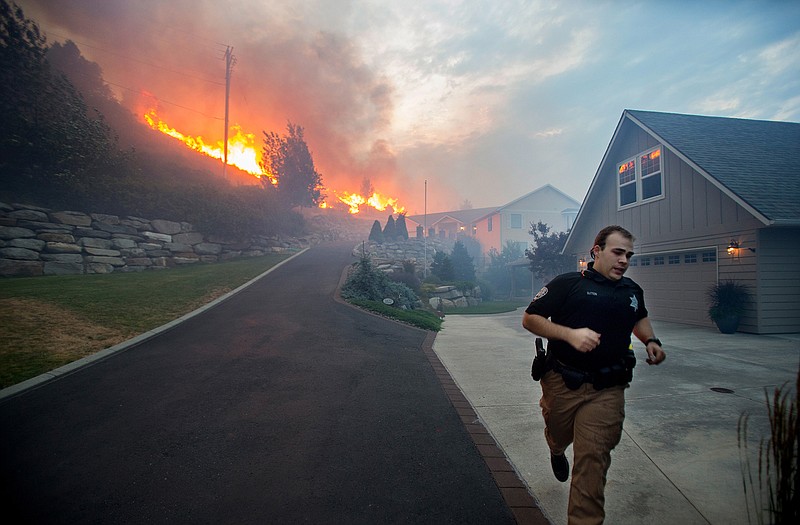 A Chelan County Sheriff's deputy races to check that all residents have left their home as flames approach houses at Quail Hollow Lane in Wenatchee, Wash. 