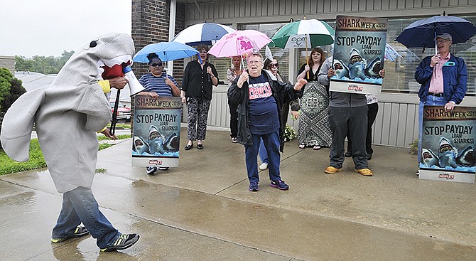 Playing off of the popular "Shark Week" theme, a man in a shark costume, along with several protestors, chanted outside U.S. Rep. Blaine Luetkemeyer's office on Wednesday in protest of so called "predatory" lenders. The coalition, made up of representatives from several advocacy groups, asked for Luetkemeyer to support legislation aimed at limiting rates by these lenders, also referred to as payday and title loan companies.