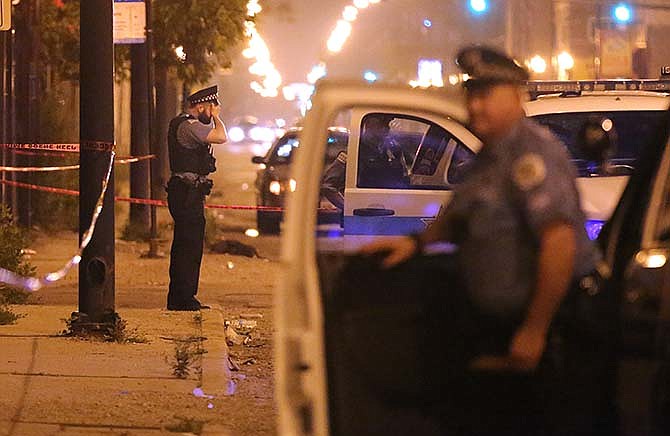 In this July 6, 2015, file photo, a Chicago police officer rests his hand on his forehead at the scene where a man was shot in the face in Chicago. Homicides and shooting incidents in Chicago are up roughly 20 percent from the same period last year. 