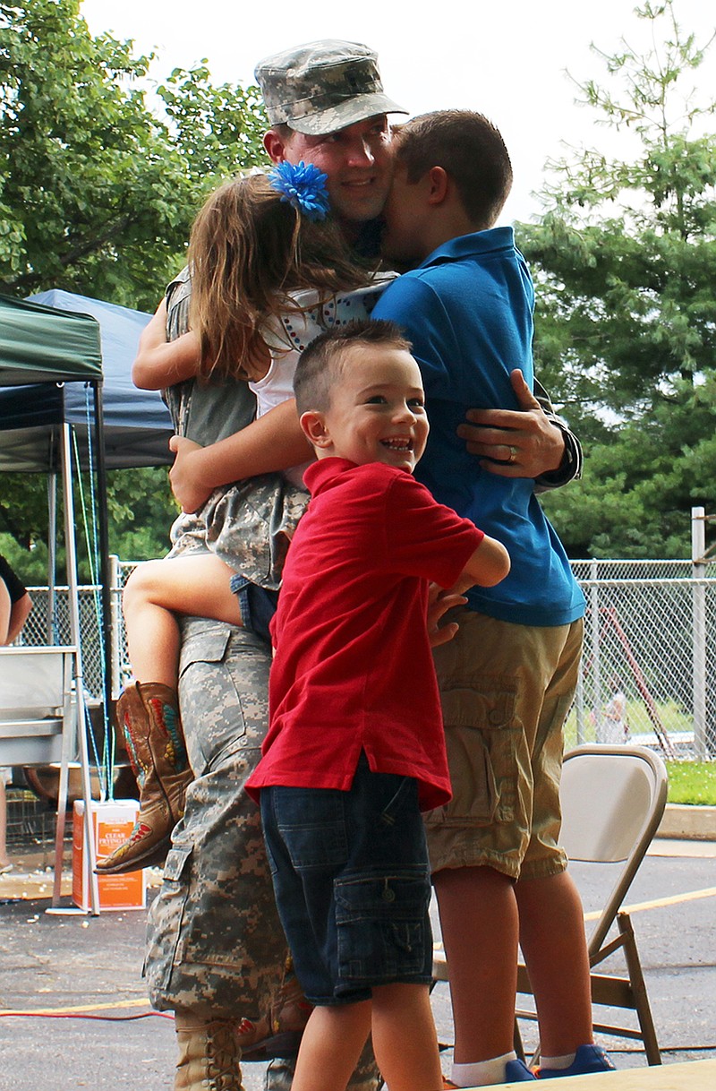 Missouri National Guard CWO2 Ryan Newlon is embraced by his children, Asher, Arabella and August, after his surprise appearance and return from Kosovo.
