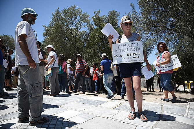 Short-term contract employees of the Culture Ministry, unpaid for over six months, inform tourists about their protest Thursday outside the entrance of the ancient Acropolis hill in Athens. Greece's radical left-led government survived another revolt by rebels in the early hours of Thursday, passing reforms that should pave the way for the imminent start of bailout discussions with European creditors. Sign reads in Greek and English "We are unpaid."