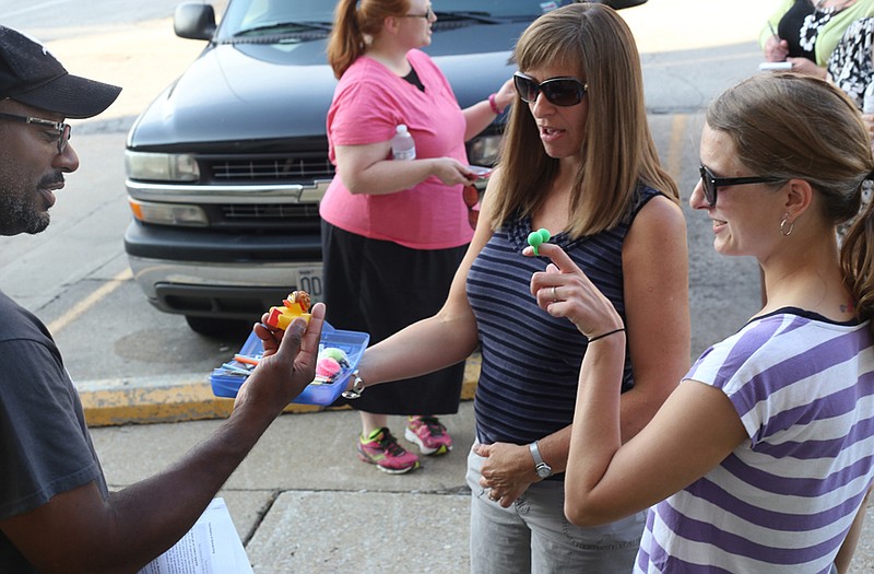 Jevon Love, left, and coordinators Lisa Sanning and Courtney Waters examine the contents of the first geocache find outside the Missouri River Regional Library on Monday.