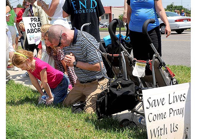 Stephen Smith of Eldon, Mo., prays with his children from left, Gracie, 9, Rachel, 4, and Claire, 6, in front of the Planned Parenthood of Kansas and Mid-Missouri during a rally Tuesday, July 28, 2015, in Columbia, Mo. About forty pro-abortion rights supporters and seventy anti-abortion supporters stood in front of the clinic holding signs as anti-abortion speakers including Mo. Rep. Diane Franklin and Missouri gubernatorial candidate Catherine Hanaway called on state and federal officials to investigate and defund Planned Parenthood.