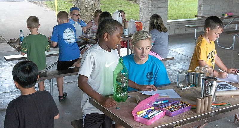 Art Camp Coordinator Melissa Gerhart, center in blue shirt, assists a young artist in choosing something to make out of a used plastic bottle in the afternoon "Going Green" session of the Exploring Art in the Park program on Thursday, July 23.