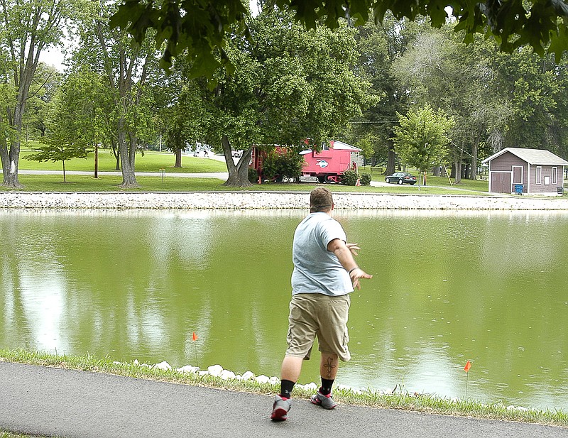 A golf disc can be seen against the red caboose and the green shrubbery as it is sent towards the hole (basket) across an arm of the the lake at Proctor Park at the membership drive tournament on Saturday, July 18. The basket is visible between two trees to the left of the caboose.