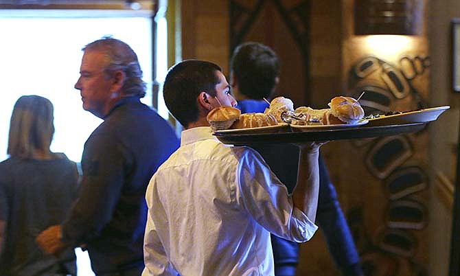 In this photo taken Monday, July 27, 2015, server Zachary DeYoung carries a tray of food at an Ivar's restaurant in Seattle. After Seattle's new minimum wage law took effect last April 1, Ivar's Seafood Restaurants announced that it was jacking up its prices by about 21 percent, eliminating tipping as a routine procedure, and immediately paying all its hourly workers a $15 per hour. They began the new pay rate three years earlier than the law required. 