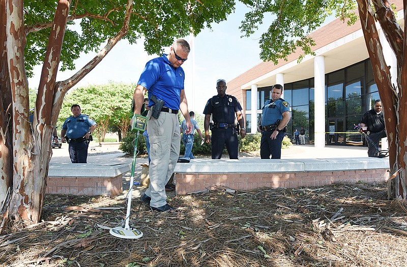 Investigators search for a shell casing along the perimeter of a pedestrian plaza outside the Madison County Courthouse in Canton, Miss.,  after a shooting on Monday, Aug. 3, 2015. A man fatally shot a defendant waiting in a small courtyard outside the county courthouse. A suspect is in custody, law enforcement officials said.