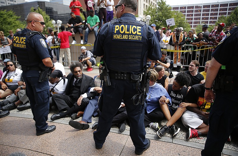 Protesters sit on the steps of the Eagleton Federal Courthouse in St. Louis as Federal Protective Service officers stand watch on Monday.