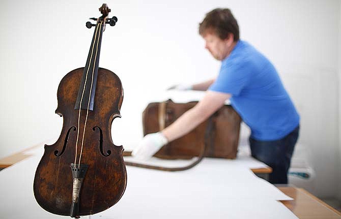 In this Sept. 16, 2013 file photo, Sean Madden, of Fine Art Conservation, works to show the violin played by bandmaster Wallace Hartley during Titanic's tragic maiden voyage, during a photocall to the media in Lurgan, Northern Ireland. The sea-corroded violin believed to have been played by the bandmaster of the Titanic as the ocean liner sank will be displayed next year at a pair of U.S. museums; from March 7 to May 29 in Branson, Missouri, and from June 5 to Aug. 14 in Pigeon Forge, Tennessee.