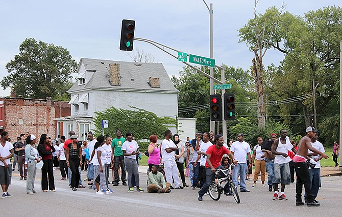 People gather at the scene of a fatal officer-involved shooting at Walton Avenue and Page Boulevard Wednesday in St. Louis. An armed man fleeing from officers serving a search warrant at a home in a crime-troubled section of north St. Louis was shot and killed by police after he pointed a gun at them, the police chief said. 