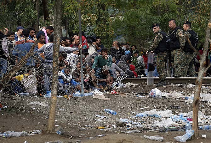 Migrants stand behind the barbed wire set by Macedonian police to stop thousands of migrants entering Macedonia illegally from Greece, near the southern Macedonian town of Gevgelija, Saturday, Aug. 22, 2015. About 39,000 people, mostly Syrian migrants, have been registered as passing through Macedonia in the past month, twice as many as the month before. 