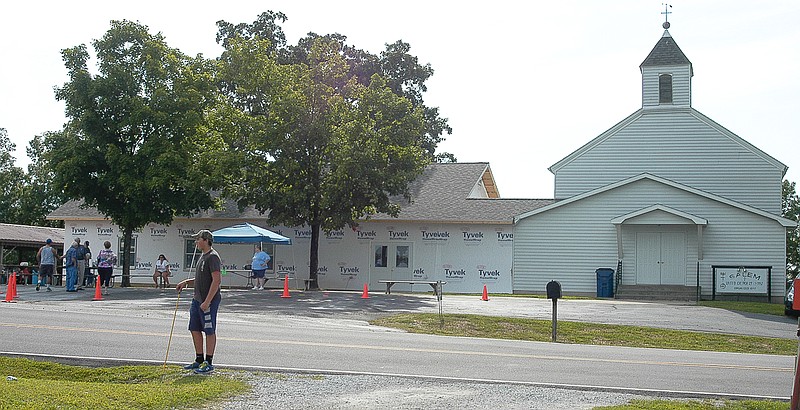 The partially completed fellowship hall is to the left of the Salem UCC Church, which was built in 1858. Standing across the highway from the church is one of a number of young people helping with car parking.