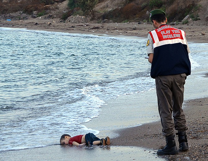 A paramilitary police officer investigates the scene before carrying the lifeless body of Aylan Kurdi, 3, after a number of migrants died and a smaller number were reported missing after boats carrying them to the Greek island of Kos capsized, near the Turkish resort of Bodrum early Wednesday.