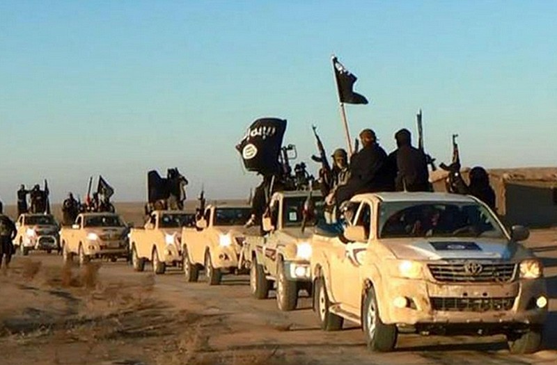 Militants of the Islamic State group hold up their weapons and wave flags as they ride in a convoy, which includes multiple Toyota pickup trucks through Syria.
