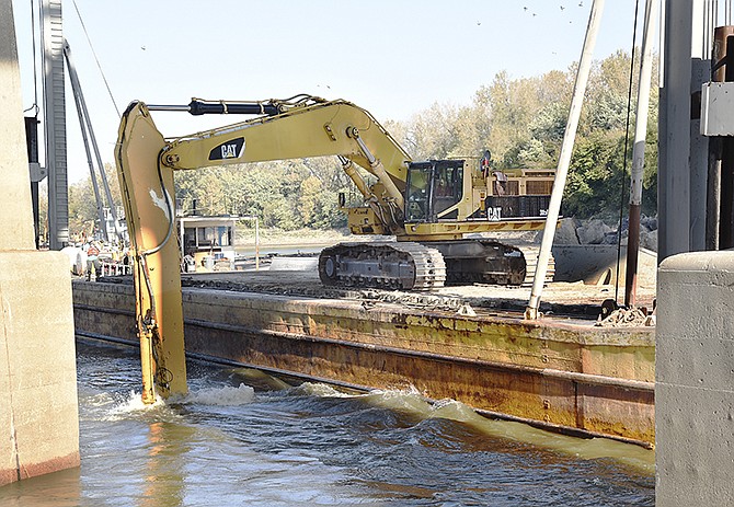 An operator from Luhr Bros. Inc. of Columbia, Illinois, use a trackhoe to move boulders on the barge and then set them in the water on top of large bags of a fine chat material. The large rocks will hold the bags in place to prevent further scouring of the bridge piers.