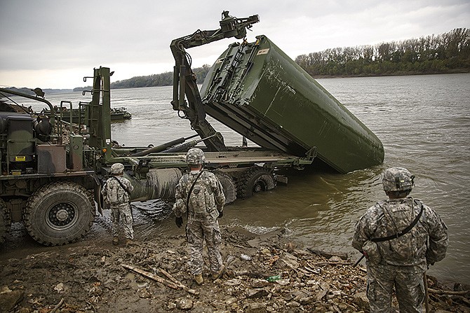 A folded section of bridge is hoisted via pneumatic arm onto the bed of a transport truck. Members of the U.S. Army 50th Multi-Role Bridge Company of Fort Leonard Wood operated a training mission in fast-moving current Wednesday at the Missouri National Guard Ike Skelton Training Site.