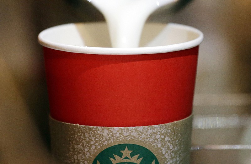 A barista pours steamed milk into a red paper cup while making an espresso drink at a Starbucks coffee shop.
