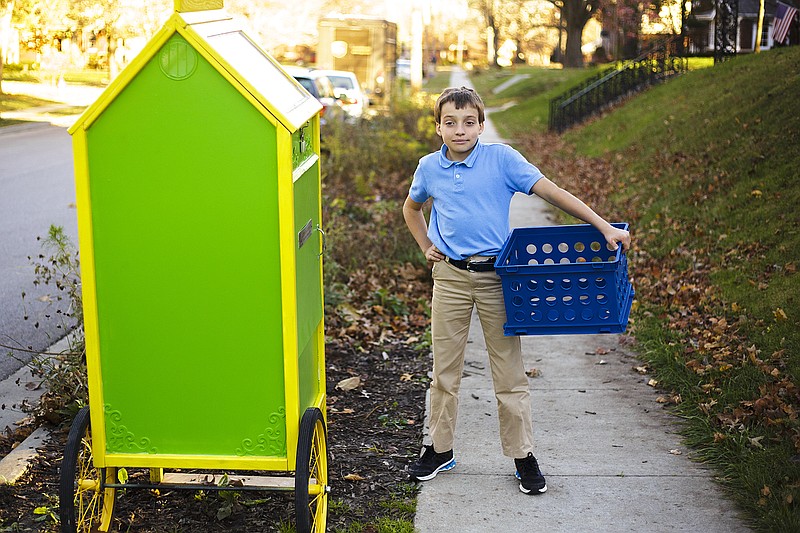 Fifth-grader David Hofherr places a crateload of books in the first of his free Little Library kiosks near his family's home on Elmerine Avenue. After repainting donated newspaper machines, Hofherr plans to set up multiple locations for these take-a-book, leave-a-book operations.