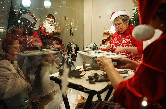 Andrea Cleeton, second from right, arranges pieces of glass while demonstrating her fused glass artwork techniques for passersby as they stop and watch through the window at Midwest Travel Consultants during Friday night's Living Windows in downtown Jefferson City. Cleeton is the new artist at The Village Art Studio at 1507 E. McCarty St.