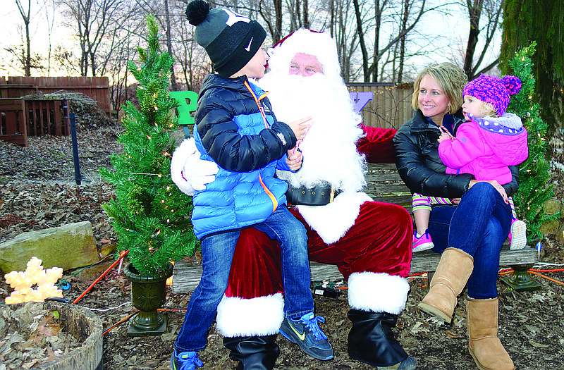 Grayson Moore, 7, sits on Santa's lap, telling him what he would like for Christmas. Meanwhile, his shy sister, Maren, 2, prefers sticking with the safety of Mom (Sally Moore) during the Master Gardeners' second annual appearance of Santa at Quigg Commons in North Jefferson City.