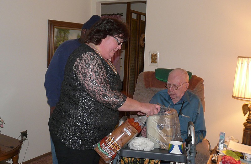 Lynn Beasley, left, and Herman Johnson (hidden) deliver some food items to Clarence Voss (seated). Voss, 92, said the home-delivered meals and fresh food items help him stay in the home he built 40 years ago rather than go to a nursing home.
