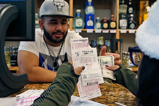 Samir Akhter, the owner of Penn Branch Liquor, exchanges money for Powerball tickets, Saturday, Jan. 9, 2016 in Washington. Officials say it's increasingly likely that someone will win the $900 million Powerball jackpot, which grew by $100 million just hours before Saturday night's drawing. 