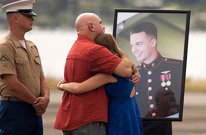 Unidentified family members gather around a photograph of U.S. Marine Lance Cpl. Ty L. Hart, 21, of Aumsville, Ore., during a memorial service for the 12 Marines who died when their helicopters crashed off the North Shore of Oahu, Hawaii, Friday Jan. 22, 2016, at Marine Corps Base Hawaii. Servicemen draped flight gear on 12 white crosses Friday to commemorate the Marines who died when two helicopters crashed off the coast of Hawaii during a nighttime training mission. Military members and families gathered for the memorial service at Marine Corps Base Hawaii in Kaneohe after the status of the dozen missing Marines changed to deceased following five days of searching. 