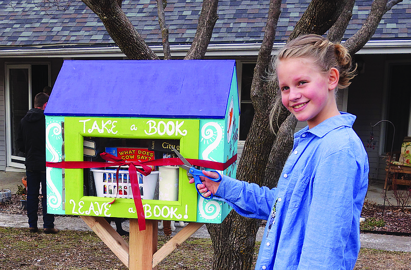 Emma Huett, 11, cuts the ribbon at the opening of Emma's Free Little Library on Sunday. The public is invited to take and leave books at the library, which was stocked with about 50 books for the opening.