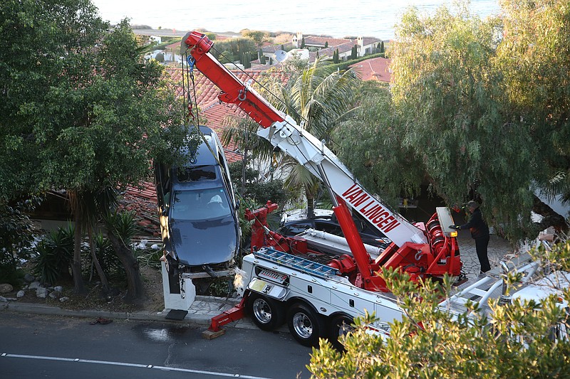 A crane removes a car that crashed off Palos Verdes Drive west and ended up on the roof of a home in Palos Verdes Estates, Calif. Wednesday, Feb. 3, 2016. Firefighters pulled the man from the damaged car and took him to a hospital, but he wasn't seriously hurt, and no one else was injured.