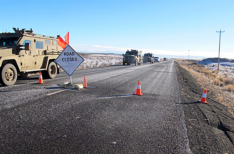 A convoy of armored vehicles and SUVs rolls past a barricade on the road near the Malheur National Wildlife Refuge near Burns, Oregon, last month. 
