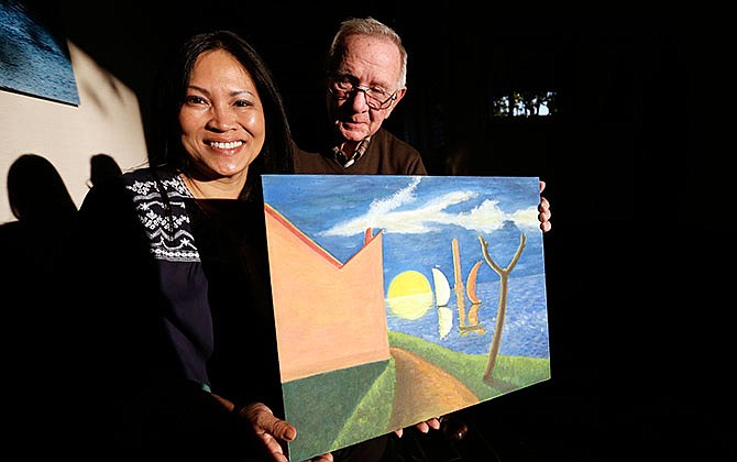 In this Jan. 12, 2016 photo, Erika Colligan poses with former Air Force instructor, retired Col. Billy Mobley as she holds a painting made by her father in San Diego. After three decades searching for her father's artwork - paintings the South Vietnam pilot made for the U.S. Air Force aviators who trained him during the Vietnam war, Colligan recently found one. The painting gave her the first tangible sliver of the father she never got the chance to know.