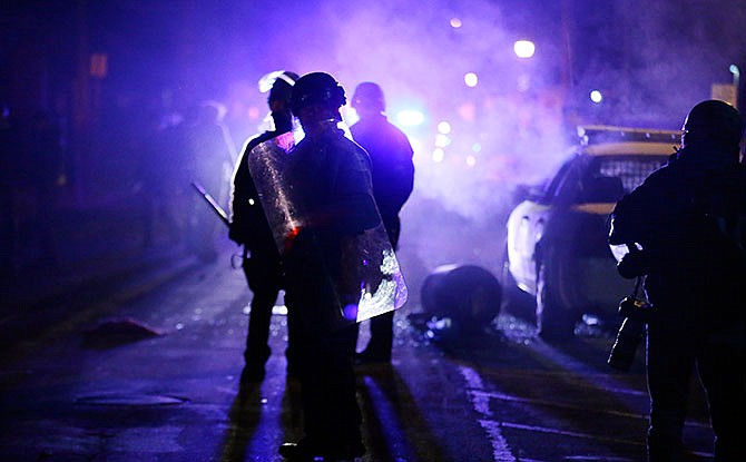 In this Nov. 25, 2014 file photo, police officers watch protesters as smoke fills the streets in Ferguson, Mo. Ferguson city leaders have spent months negotiating a settlement with the U.S. Department of Justice, a plan that calls for sweeping changes in policing practices in the St. Louis suburb. Now, residents get their say. The first of three public meetings on the proposed consent decree is Tuesday, Feb. 2, 2016 at Ferguson City Hall.