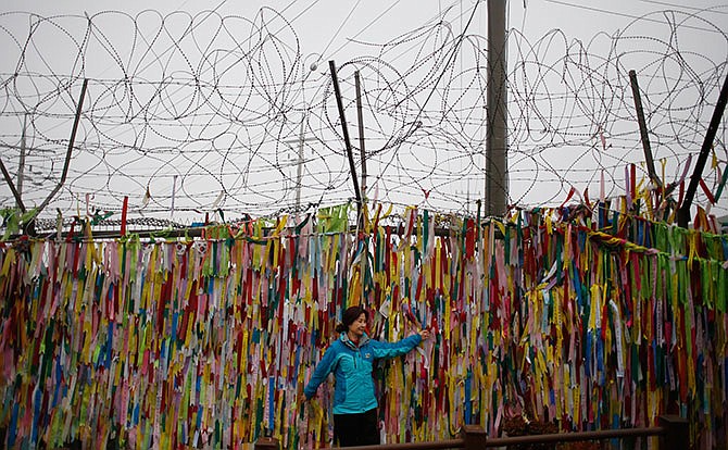 A woman poses for a souvenir photo in front of ribbons hanging on a wire fence for the reunification of the two Koreas at the Imjingak Pavilion near the border village of Panmunjom in Paju, South Korea, Friday, Feb. 12, 2016.