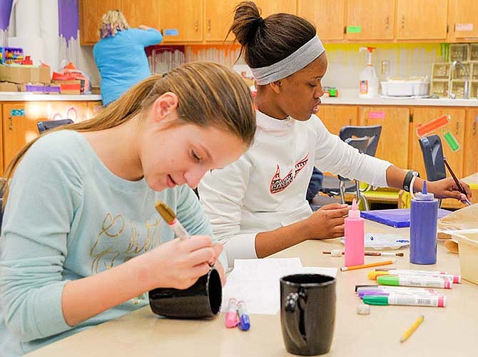 Mallory Adrian, left, works on a matching set of coffee mugs while Lamajah Johnson paints a wall canvas with a quote. These items are for a silent auction Thursday at Eugene Elementary School to help fund the students publishing meat and dairy signs to be displayed at Fairway grocery store.