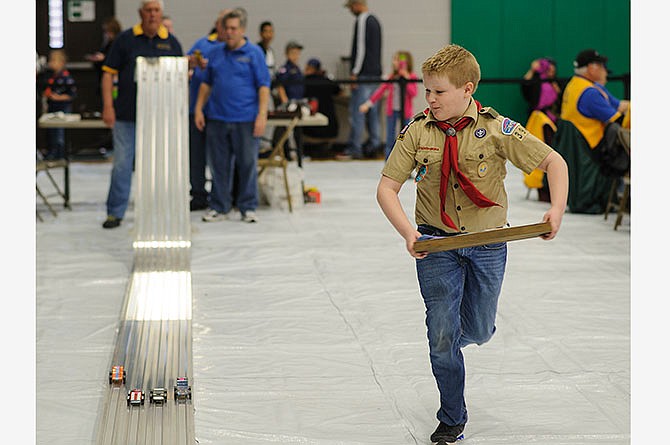 Troop 394 Boy Scout Jack Allmeroth tries to outrun cars competing in the Bear den heat races Saturday after he returned the previous heat's cars to the starting area during the Five Rivers District Cub Scout Pinewood Derby at Blair Oaks Middle School in Wardsville, Mo.