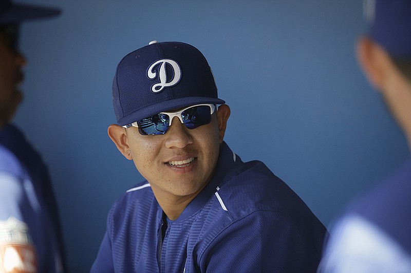 In this photo taken Monday, March 14, 2016, Los Angeles Dodgers starting pitcher Julio Urias smiles while talking to teammates in the dugout during the team's spring training baseball game against the Milwaukee Brewers in Phoenix. Spanish-speaking players from Latin America usually struggle with a new language. MLB instructed its 30 teams this season to hire full-time Spanish interpreters for their Latin players. 