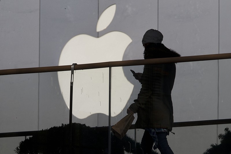 In this Dec. 23, 2013, file photo, a woman using a phone walks past Apple's logo near its retail outlet in Beijing. Even while it fiercely opposes the FBI's demand for help unlocking an encrypted iPhone used in the San Bernardino mass shootings, Apple has never argued that it isn't capable of doing what the government wants. While the FBI may have found an alternative solution in the San Bernardino case, experts say it's almost certain that Apple and other tech companies will keep increasing the security of their products, making it harder or perhaps even impossible for them to answer government demands for customers' data.