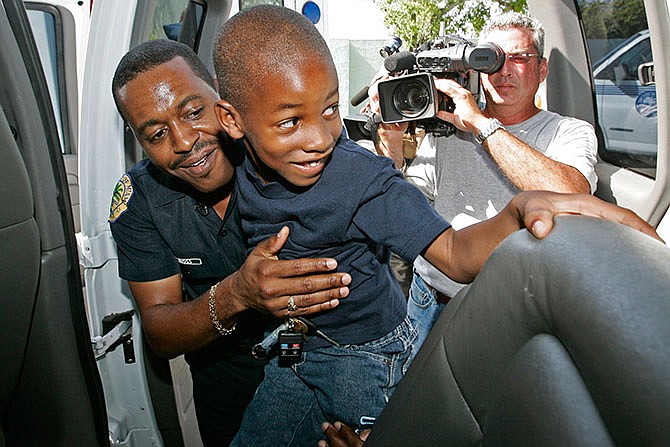 In this Aug. 9, 2006 photo, Miami police officer Delrish Moss, helps David Jenkins into the van in Miami, taking the family to Disney World. Thanks to donations from the community the family of Sherdavia Jenkins, who was shot in front of her home, traveled to Disney World. Moss was announced as police chief in Ferguson, Mo., Thursday, March 31, 2016, putting a black man in charge of a mostly white department that serves a town where African-Americans make up two-thirds of the residents. (Al Diaz/The Miami Herald via AP)