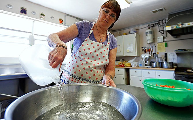 In this Feb. 29, 2016 photo, Sandra Porter, the cook and water operator at Ozark Action Head Start in Ava, Mo., pours a gallon of bottled water into a bowl while she cooks for the children attending Ava Head Start. Buying bottled water for drinking has been the routine at Ava Head Start even before lead levels spiked after moving into a new center in 2010. But it wasn't until February, after another round of high tests results, that state regulators told the preschool to use bottled water for cooking and cleaning the toothbrushes for the 59 children, age 3 and 4, said Porter. (Guillermo Hernandez Martinez/The Springfield News-Leader via AP)