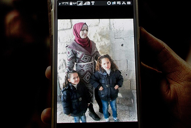 Palestinian Taghreed Taha, 25, the sister of Maram, 24 and Ibrahim Taha, 16, displays a photo Thursday of her sister Maram and her tow daughters, Rimas, 4, left and Sarah, 5, right, on her mobile phone, at the family house, in the West Bank village of Qatana, near Ramallah.