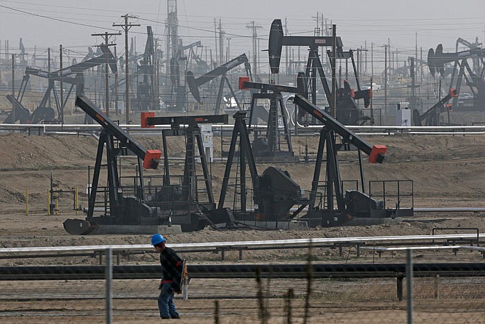 In this Jan. 16, 2015, file photo, a person walks past pump jacks operating at the Kern River Oil Field in Bakersfield, Calif. 