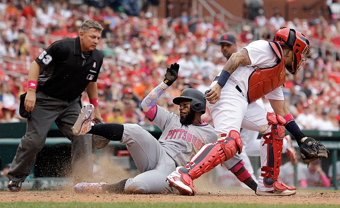 Pittsburgh Pirates' Josh Harrison, center, scores past St. Louis Cardinals catcher Yadier Molina, right, and home plate umpire Greg Gibson, left, during the ninth inning of a baseball game Sunday, May 8, 2016, in St. Louis.