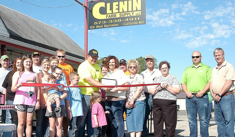 The owner of Clenin Farm Supply, Tyler Clenin, center, in the yellow shirt, cuts the Chamber of Commerce ribbon, as Chamber President Amanda Trimble, to his left in the photo, holds the "First Dollar." Many chamber members, and family and friends of Tyler are present in the photo. The event was held May 7, 2016.