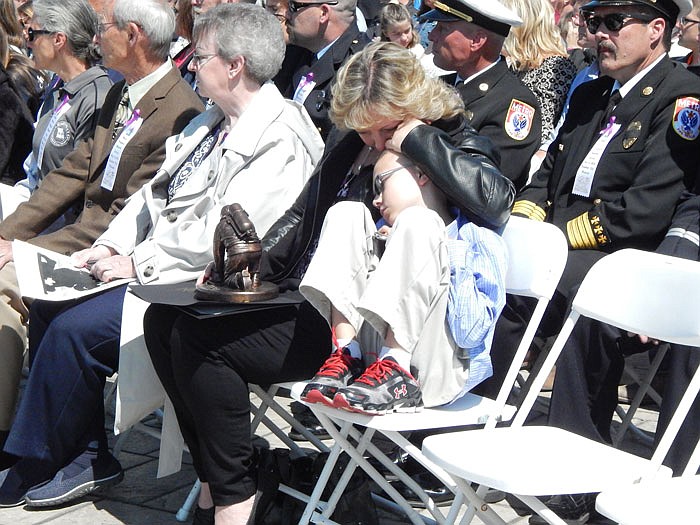 Melia Tindall comforts her child during a Sunday ceremony which recognized her husband, Christopher A. Tindall, and four other deceased firefighters. A battalion chief with South Metropolitan Fire Protection District in Raymore, he died Jan. 8, 2015, several hours after responding to an emergency call. He also was a member of the Missouri Search and Rescue K9 Unit.