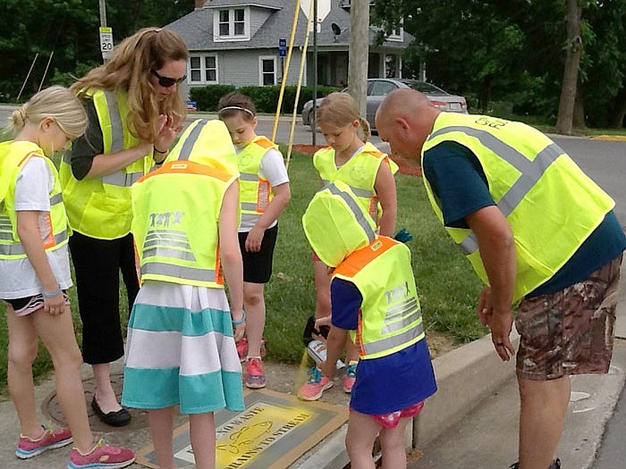 Members of Fulton Brownie Troop 71045, with leader Cindy Beckmeyer, spray paint an important message atop storm drains Monday evening. The group has been working in the area near Veterans Park with the help of Jason Woods, Fulton traffic control supervisor, to create awareness of inappropriate dumping of oil and chemicals which make their way into creeks passing through town.