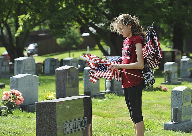 Emily Reed unrolls an American flag as she prepares to place it at a military marker near an individual's headstone as Riverview Cemetery prepares for Memorial Day visits. A member of Jefferson City High School's National Honor Society, Reed and other members put flags on hundreds of markers in the cemetery