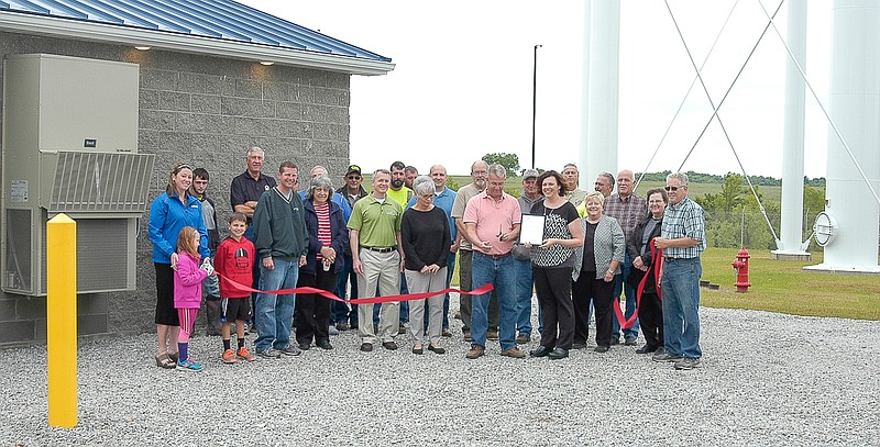 The ribbon is cut by California Mayor Norris Gerhart for the newest well, Well 9, of the City of California. The well house is the gray stone building at the left. The base of the new 600,000-gallon water tower is at the right. Holding the framed certificate of dedication is Chamber President Amanda Trimble.