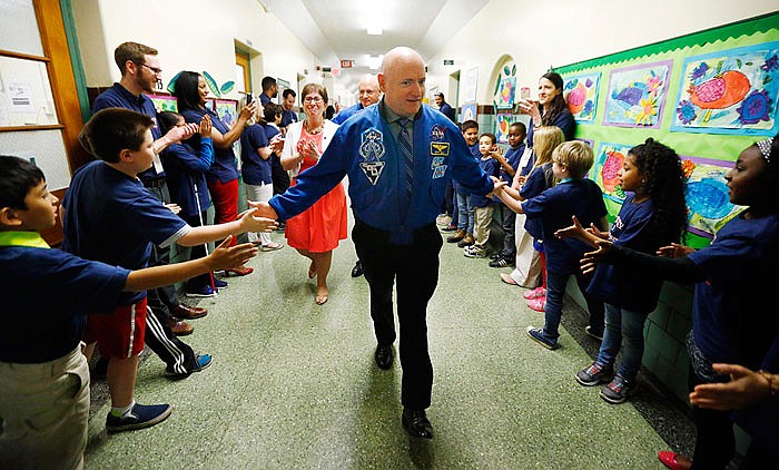 Retired astronaut Scott Kelly, center, and his twin brother Mark Kelly, back, are greeted by children in the hallway of the Kelly Elementary School after the school was named in their honor in West Orange, N.J. On Wednesday, NASA's yearlong spaceman, Scott Kelly, says even after two months back on Earth, his feet are still sore. 
